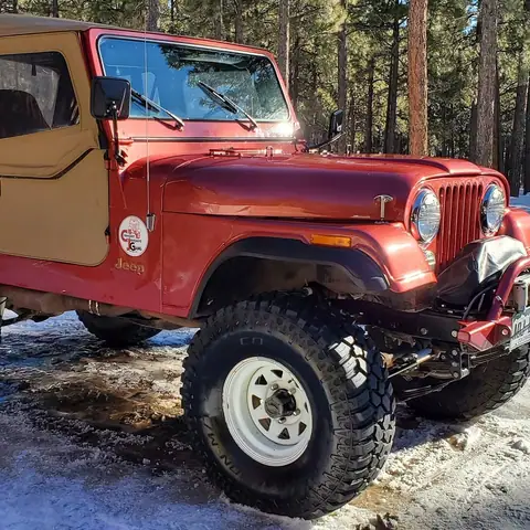 Classic red Jeep CJ-7 with a tan soft top on snowy ground