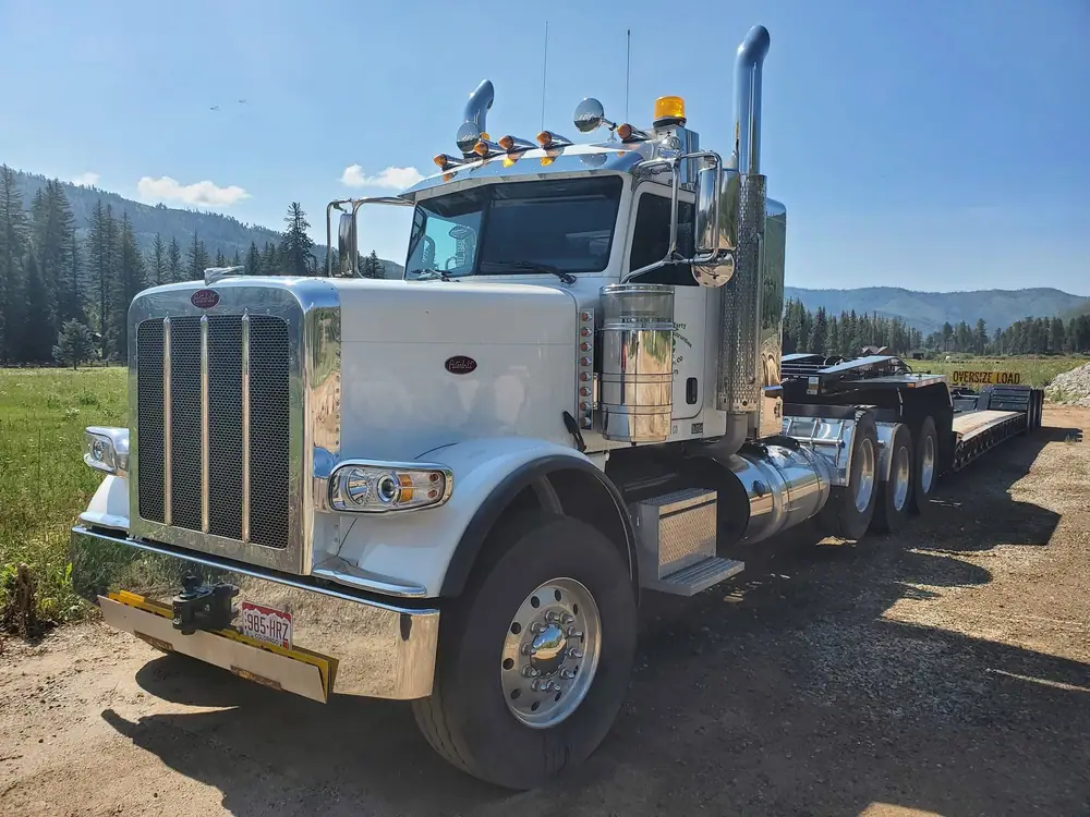 Chrome Peterbilt semi truck with a lowboy trailer, detailed in a mountain valley